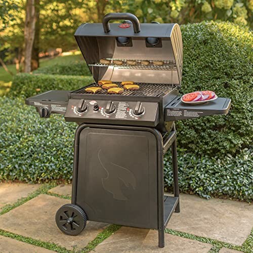 Outdoor gas grill with burgers and vegetables in a garden setting.