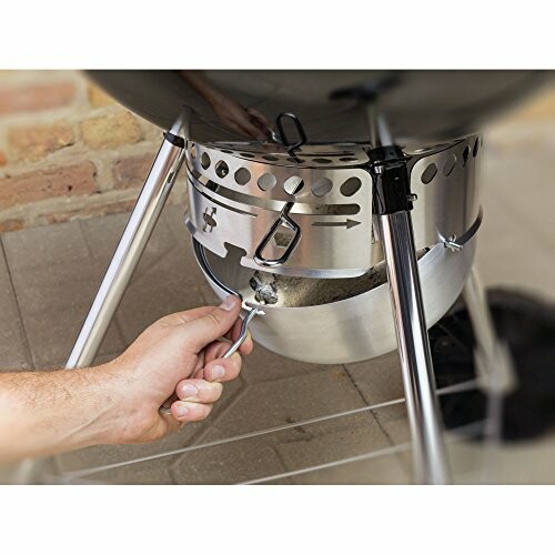 Person adjusting bottom vent of a charcoal grill.