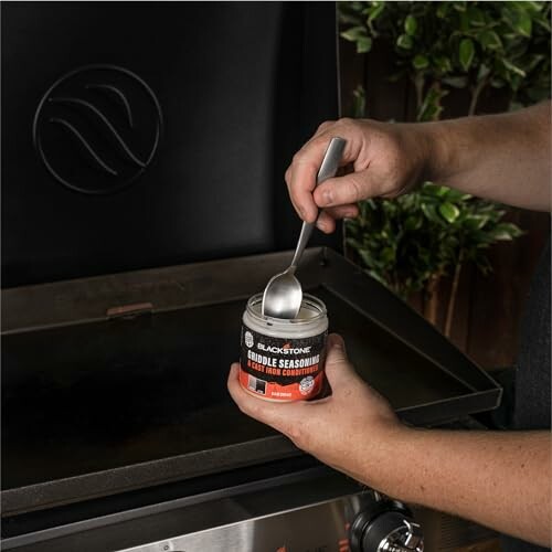 Person applying Blackstone griddle seasoning on a grill.