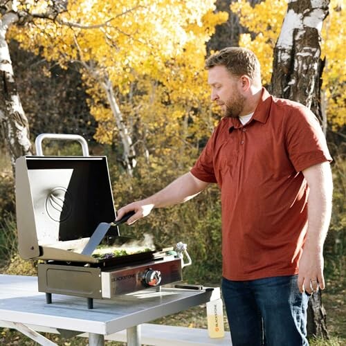 Man grilling on a portable grill in an autumn setting.