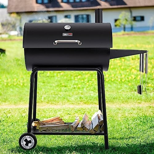 Black outdoor charcoal grill with wood storage on grass.