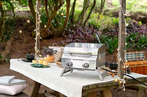 Outdoor picnic setup with a portable stainless steel grill on a table, ideal for gatherings.