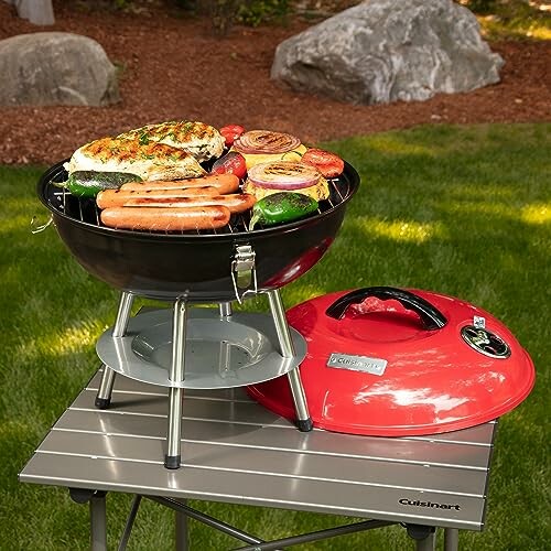 Portable charcoal grill with food on a small outdoor table.