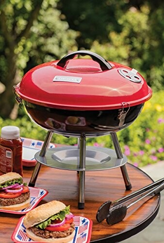 Portable charcoal grill on table with burgers and condiments.