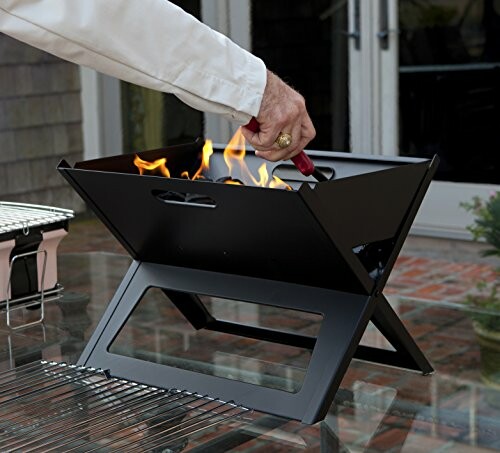 Person lighting a portable folding fire pit outdoors.