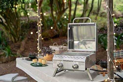 Portable grill on a table outdoors with string lights, perfect for evening gatherings.