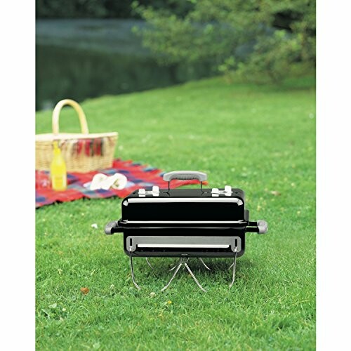 Portable grill on grass with picnic basket in background.