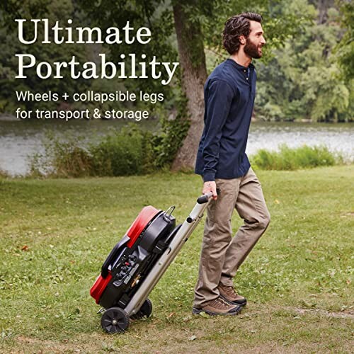 Man transporting a portable grill with wheels and collapsible legs near a lake.